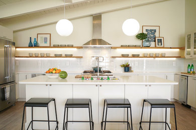 Example of a mid-century modern u-shaped medium tone wood floor and brown floor kitchen design in Baltimore with an undermount sink, flat-panel cabinets, white cabinets, white backsplash, stainless steel appliances, an island and white countertops