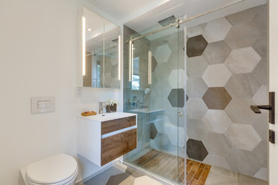 Inspiration for a mid-sized scandinavian 3/4 bathroom in Toronto with flat-panel cabinets, medium wood cabinets, an alcove shower, a wall-mount toilet, beige tile, brown tile, gray tile, multi-coloured tile, white tile, porcelain tile, white walls, porcelain floors, an integrated sink, solid surface benchtops, multi-coloured floor and a sliding shower screen.