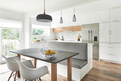 Photo of a mid-sized contemporary l-shaped eat-in kitchen in Toronto with an undermount sink, flat-panel cabinets, white cabinets, multi-coloured splashback, mosaic tile splashback, stainless steel appliances, medium hardwood floors, with island and white benchtop.