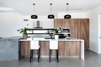 Design ideas for a contemporary kitchen in Perth with a drop-in sink, flat-panel cabinets, medium wood cabinets, black appliances, multiple islands, grey floor and white benchtop.