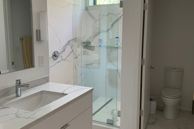 Photo of a large modern master bathroom in Burlington with white cabinets, white tile, white walls, white floor, a sliding shower screen, white benchtops, flat-panel cabinets, porcelain tile, porcelain floors, an undermount sink and engineered quartz benchtops.