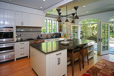 Large arts and crafts single-wall medium tone wood floor open concept kitchen photo in Boston with a drop-in sink, flat-panel cabinets, white cabinets, granite countertops, mosaic tile backsplash, stainless steel appliances and an island