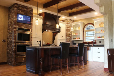 Inspiration for a large mediterranean l-shaped eat-in kitchen in St Louis with a farmhouse sink, raised-panel cabinets, white cabinets, quartz benchtops, stainless steel appliances, medium hardwood floors, with island and brown floor.