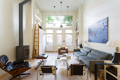Aménagement d'un salon scandinave ouvert avec une bibliothèque ou un coin lecture, un mur blanc, parquet clair, un poêle à bois, aucun téléviseur et un sol beige.