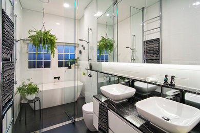 This is an example of a small contemporary master wet room bathroom in Sydney with white cabinets, white tile, white walls, a vessel sink, a hinged shower door, a freestanding tub, a one-piece toilet, subway tile, ceramic floors, marble benchtops, black floor, black benchtops and flat-panel cabinets.