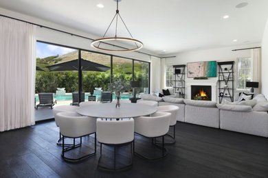 Kitchen/dining room combo - large modern dark wood floor and black floor kitchen/dining room combo idea in Orange County with white walls, a standard fireplace and a wood fireplace surround
