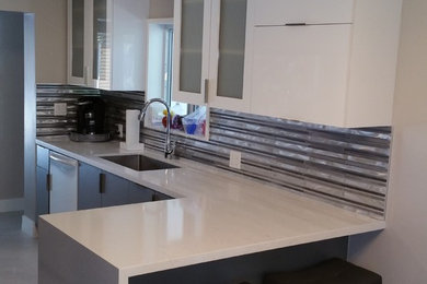Inspiration for a large modern l-shaped ceramic tile eat-in kitchen remodel in Miami with a drop-in sink, flat-panel cabinets, white cabinets, laminate countertops, gray backsplash, glass tile backsplash, stainless steel appliances and a peninsula