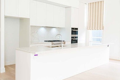 This is an example of a mid-sized modern galley eat-in kitchen in Sydney with a double-bowl sink, flat-panel cabinets, white cabinets, quartz benchtops, white splashback, light hardwood floors, with island and white benchtop.