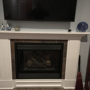 Diseño de sótano en el subsuelo tradicional, de tamaño medio, con paredes grises, suelo de madera oscura, chimenea tradicional, marco de chimenea de madera y suelo marrón