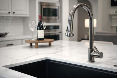 Inspiration for a mid-sized transitional medium tone wood floor and brown floor kitchen remodel in Houston with a single-bowl sink, raised-panel cabinets, quartz countertops, white backsplash, ceramic backsplash, stainless steel appliances, an island and white countertops