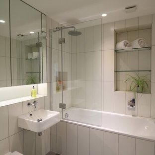 This is an example of a medium sized contemporary family bathroom in London with glass-front cabinets, a built-in bath, a shower/bath combination, a wall mounted toilet, white tiles, porcelain tiles, porcelain flooring, a wall-mounted sink, glass worktops, multi-coloured floors and a hinged door.