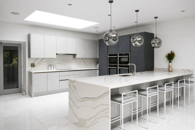 Photo of a large modern grey and white open plan kitchen in Essex with an integrated sink, flat-panel cabinets, quartz worktops, white splashback, black appliances, porcelain flooring, an island and white worktops.