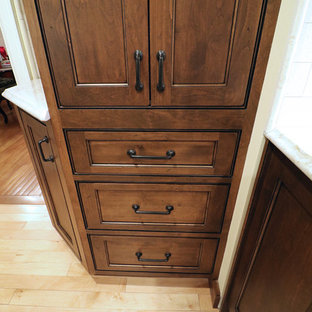 Photo of a mid-sized arts and crafts l-shaped kitchen pantry in Boston with a farmhouse sink, beaded inset cabinets, dark wood cabinets, quartz benchtops, beige splashback, travertine splashback, stainless steel appliances, light hardwood floors, no island and beige floor.