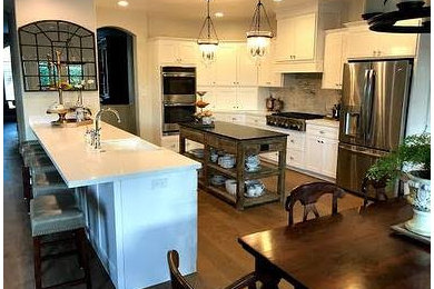Large transitional l-shaped light wood floor and brown floor eat-in kitchen photo in Other with a farmhouse sink, shaker cabinets, white cabinets, quartzite countertops, white backsplash, marble backsplash, stainless steel appliances and an island