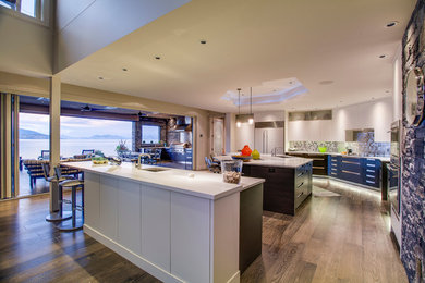 Photo of a large contemporary open plan kitchen in Vancouver with an integrated sink, flat-panel cabinets, white cabinets, granite benchtops, green splashback, glass tile splashback, stainless steel appliances, light hardwood floors and multiple islands.