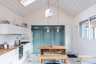 Aménagement d'une grande cuisine ouverte linéaire et encastrable contemporaine avec un évier 2 bacs, un placard à porte affleurante, des portes de placard blanches, un plan de travail en bois, une crédence blanche, une crédence en céramique, carreaux de ciment au sol et un sol blanc.