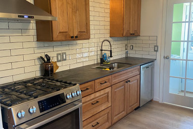Example of a mid-sized trendy laminate floor and brown floor kitchen design in Portland with an undermount sink, raised-panel cabinets, medium tone wood cabinets, solid surface countertops, white backsplash, ceramic backsplash, stainless steel appliances and multicolored countertops