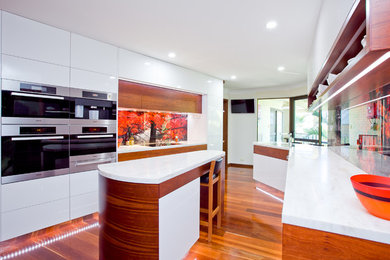 Photo of a large modern galley separate kitchen in Perth with with island, flat-panel cabinets, white cabinets, multi-coloured splashback, glass sheet splashback, stainless steel appliances, a double-bowl sink, solid surface benchtops, dark hardwood floors and brown floor.