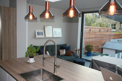 This is an example of a small classic single-wall kitchen/diner in London with a built-in sink, flat-panel cabinets, white cabinets, wood worktops, an island and feature lighting.