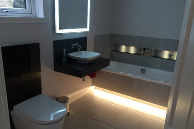 This is an example of a medium sized contemporary family bathroom with a built-in bath, a wall mounted toilet, porcelain tiles, porcelain flooring, a console sink, solid surface worktops, grey tiles and grey walls.