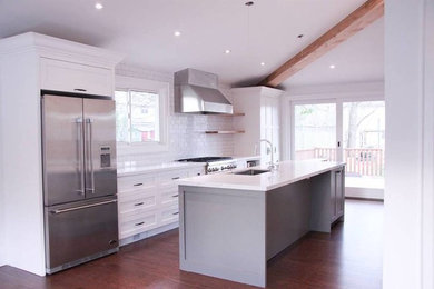 Inspiration for a mid-sized transitional galley open plan kitchen in Toronto with an undermount sink, recessed-panel cabinets, white cabinets, quartz benchtops, white splashback, subway tile splashback, stainless steel appliances, dark hardwood floors, with island and brown floor.