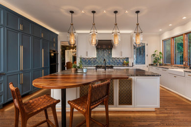 Inspiration for a transitional u-shaped medium tone wood floor and brown floor eat-in kitchen remodel with a farmhouse sink, recessed-panel cabinets, blue cabinets, granite countertops, blue backsplash, glass tile backsplash, paneled appliances, an island and brown countertops