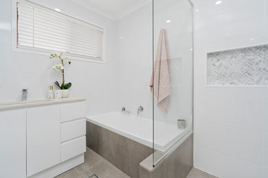 This is an example of a modern bathroom in Brisbane with a drop-in tub, white tile, ceramic tile, white walls, ceramic floors, an undermount sink, engineered quartz benchtops, beige floor and beige benchtops.