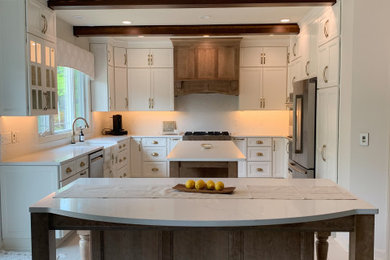 Example of a large tuscan l-shaped ceramic tile, white floor and exposed beam enclosed kitchen design in Other with a farmhouse sink, recessed-panel cabinets, white cabinets, quartz countertops, white backsplash, quartz backsplash, stainless steel appliances, two islands and white countertops