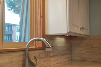 This is an example of a small transitional galley separate kitchen in Seattle with an undermount sink, raised-panel cabinets, white cabinets, solid surface benchtops, beige splashback, stone tile splashback, white appliances, porcelain floors and no island.