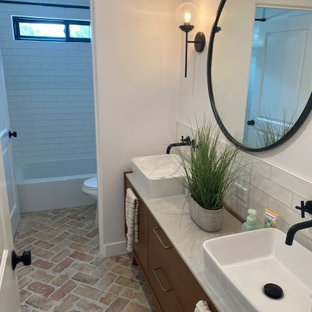Mid-sized transitional kids bathroom in Los Angeles with flat-panel cabinets, medium wood cabinets, an alcove tub, a shower/bathtub combo, a one-piece toilet, white tile, ceramic tile, white walls, brick floors, a vessel sink, granite benchtops, red floor, a shower curtain, white benchtops, a double vanity and a freestanding vanity.