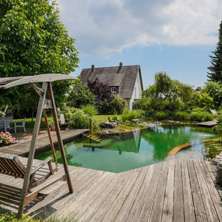 Exempel på en stor lantlig anpassad baddamm längs med huset, med trädäck