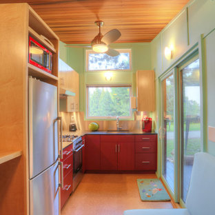 Свежая идея для дизайна: маленькая угловая кухня-гостиная в стиле модернизм с врезной раковиной, плоскими фасадами, красными фасадами, столешницей из акрилового камня, техникой из нержавеющей стали и пробковым полом без острова - отличное фото интерьера