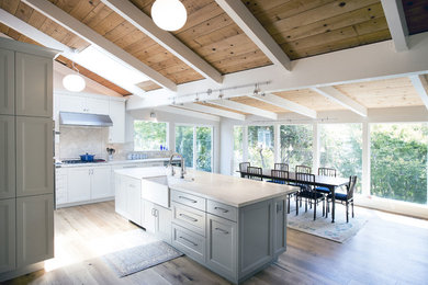 Eat-in kitchen - huge contemporary l-shaped medium tone wood floor and brown floor eat-in kitchen idea in Other with a farmhouse sink, recessed-panel cabinets, white cabinets, quartz countertops, beige backsplash, travertine backsplash, stainless steel appliances, an island and white countertops