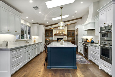 Huge transitional galley medium tone wood floor, brown floor and vaulted ceiling open concept kitchen photo in San Francisco with a farmhouse sink, beaded inset cabinets, white cabinets, quartzite countertops, white backsplash, ceramic backsplash, stainless steel appliances, an island and white countertops