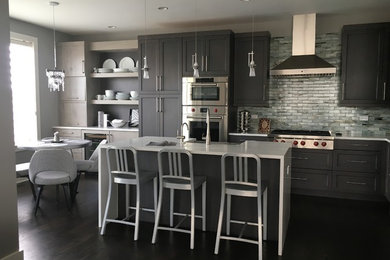 Mid-sized trendy u-shaped dark wood floor and brown floor eat-in kitchen photo in Chicago with a farmhouse sink, recessed-panel cabinets, gray cabinets, quartz countertops, gray backsplash, subway tile backsplash, stainless steel appliances, an island and white countertops