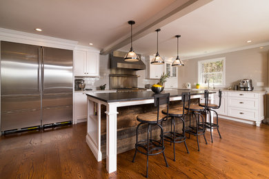 Example of a mid-sized minimalist l-shaped dark wood floor kitchen design in Boston with a farmhouse sink, shaker cabinets, white cabinets, solid surface countertops, gray backsplash, subway tile backsplash, stainless steel appliances and an island