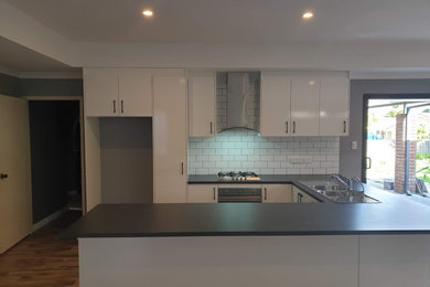Inspiration for a mid-sized u-shaped open plan kitchen in Perth with white cabinets, laminate benchtops, white splashback, subway tile splashback, stainless steel appliances, vinyl floors, brown floor and black benchtop.