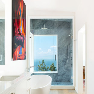 Inspiration for a contemporary light wood floor and beige floor bathroom remodel in Sacramento with recessed-panel cabinets, white cabinets, white walls, an undermount sink, a hinged shower door and white countertops