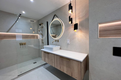 Inspiration for a large modern ensuite wet room bathroom in London with freestanding cabinets, medium wood cabinets, a bidet, grey tiles, porcelain tiles, grey walls, porcelain flooring, a wall-mounted sink, engineered stone worktops, grey floors, an open shower, white worktops, a feature wall, a single sink and a floating vanity unit.