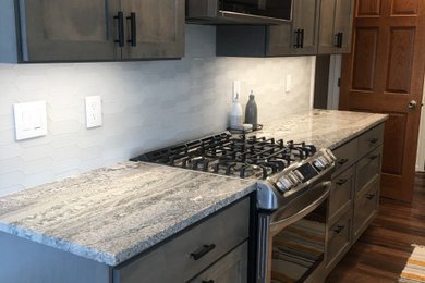 Example of a mid-sized trendy galley vinyl floor and brown floor eat-in kitchen design in Minneapolis with a farmhouse sink, shaker cabinets, gray cabinets, quartzite countertops, white backsplash, glass tile backsplash, stainless steel appliances and gray countertops