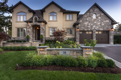 Mid-sized traditional two-storey beige exterior in Toronto with stone veneer and a clipped gable roof.