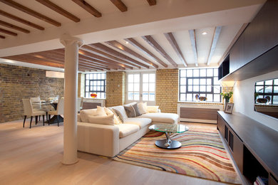 This is an example of a mid-sized contemporary loft-style living room in London with a library, white walls, light hardwood floors and a wall-mounted tv.