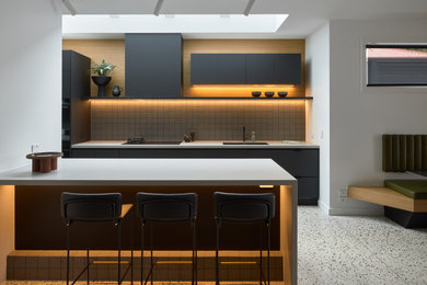 Photo of a large contemporary kitchen in Melbourne with flat-panel cabinets, black cabinets, solid surface benchtops, grey splashback, mosaic tile splashback, black appliances, concrete floors, with island, multi-coloured floor and grey benchtop.