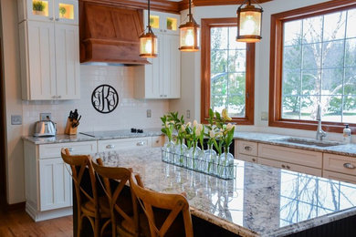 Example of a large transitional l-shaped enclosed kitchen design in Cleveland with shaker cabinets, white cabinets, granite countertops, white backsplash, subway tile backsplash and an island