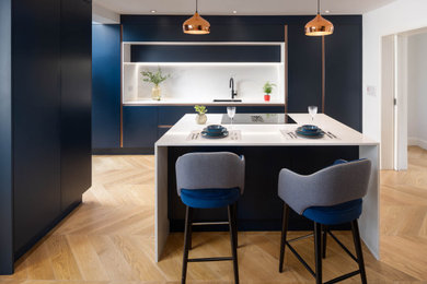 Example of a mid-sized trendy l-shaped light wood floor and yellow floor open concept kitchen design in Dublin with a double-bowl sink, flat-panel cabinets, blue cabinets, quartz countertops, white backsplash, quartz backsplash, black appliances, an island and white countertops