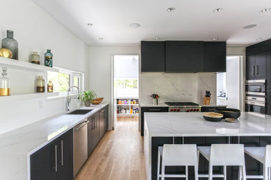 This is an example of a mid-sized contemporary u-shaped eat-in kitchen in New York with an undermount sink, flat-panel cabinets, blue cabinets, quartz benchtops, white splashback, stone slab splashback, light hardwood floors, with island, white benchtop and stainless steel appliances.