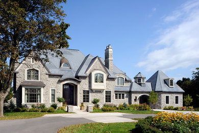 Example of a large classic gray two-story stone gable roof design in Toronto