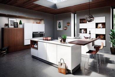 This is an example of a mid-sized l-shaped eat-in kitchen in Calgary with a single-bowl sink, flat-panel cabinets, white cabinets, quartzite benchtops, black appliances, concrete floors, multiple islands, grey floor and white benchtop.