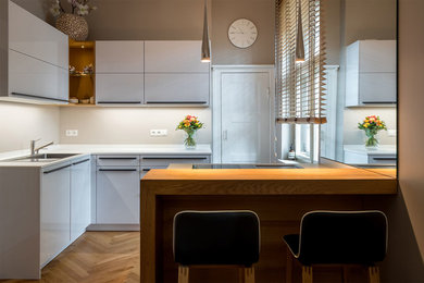 Mid-sized contemporary l-shaped open plan kitchen in Berlin with a single-bowl sink, flat-panel cabinets, white cabinets, panelled appliances, a peninsula and white benchtop.