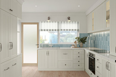 Inspiration for a small coastal l-shaped open plan kitchen in Melbourne with a submerged sink, recessed-panel cabinets, white cabinets, engineered stone countertops, blue splashback, ceramic splashback, black appliances, light hardwood flooring, brown floors and multicoloured worktops.